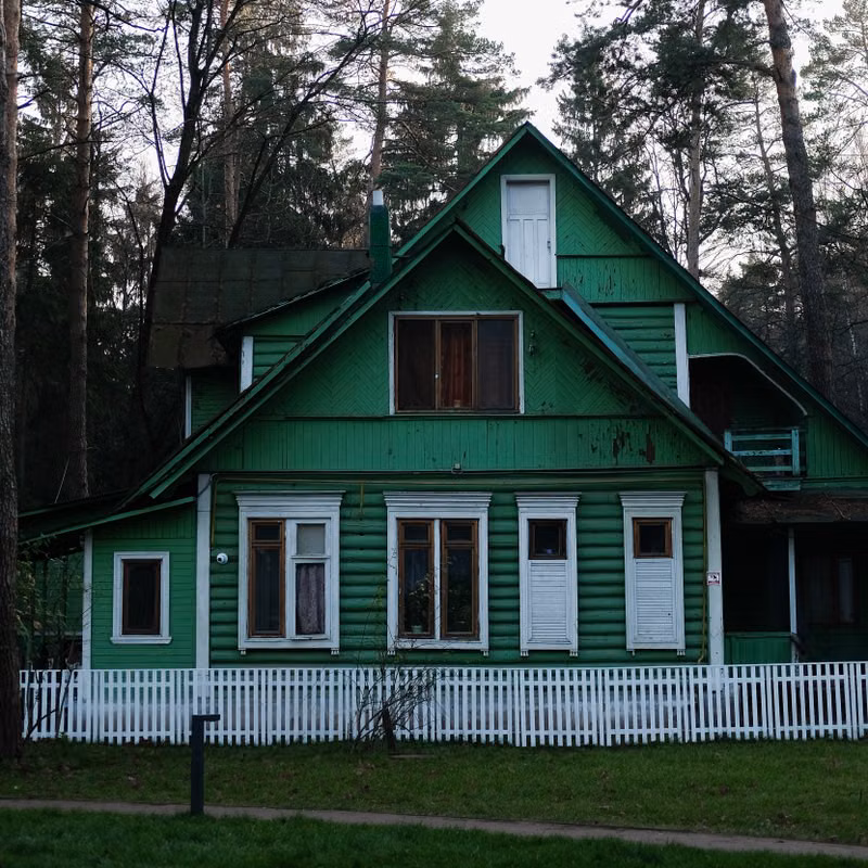 A scenic view of a green wooden house surrounded by forest in Russia.